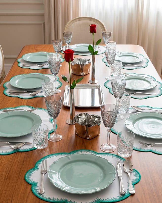 Mesa posta da Maria Pia Casa com pratos verdes, taças de cristal e rosas vermelhas.