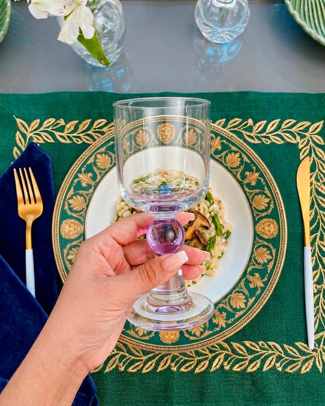 Taça de cristal segurada sobre prato decorado em verde e dourado, da Maria Pia Casa.